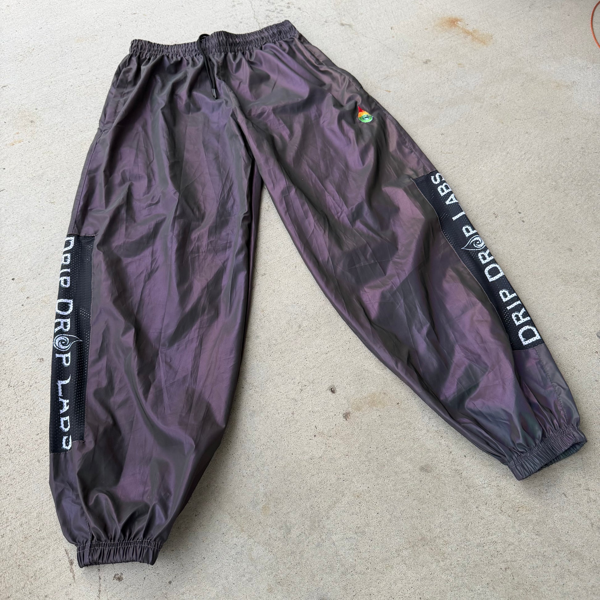 Reflective parachute pants by Drip Drop Labs showing shiny, lightweight fabric with adjustable waist and tapered legs.