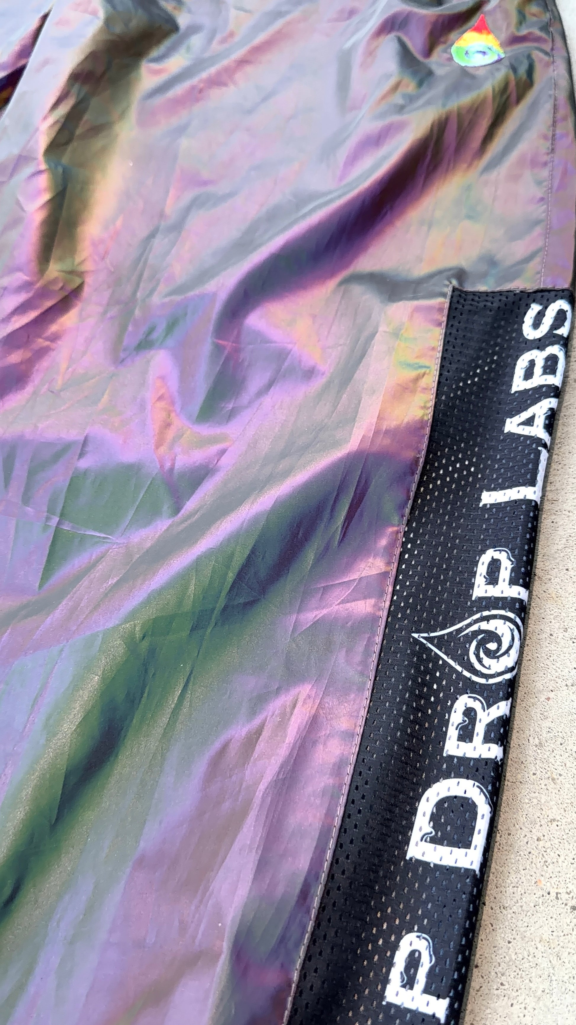 Reflective parachute pants by Drip Drop Labs featuring shiny fabric and adjustable drawstring waist for a stylish, functional look.